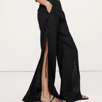 Person wearing black wide-leg pants with a high slit on a white background