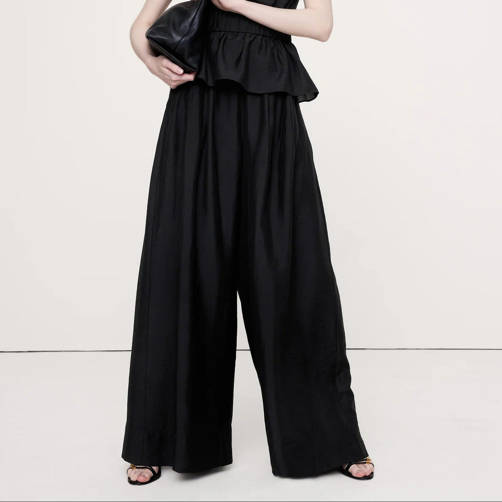 Woman wearing a black strapless jumpsuit holding a clutch on a white background