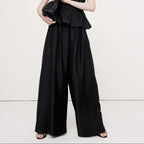 Woman wearing a black strapless jumpsuit holding a clutch on a white background