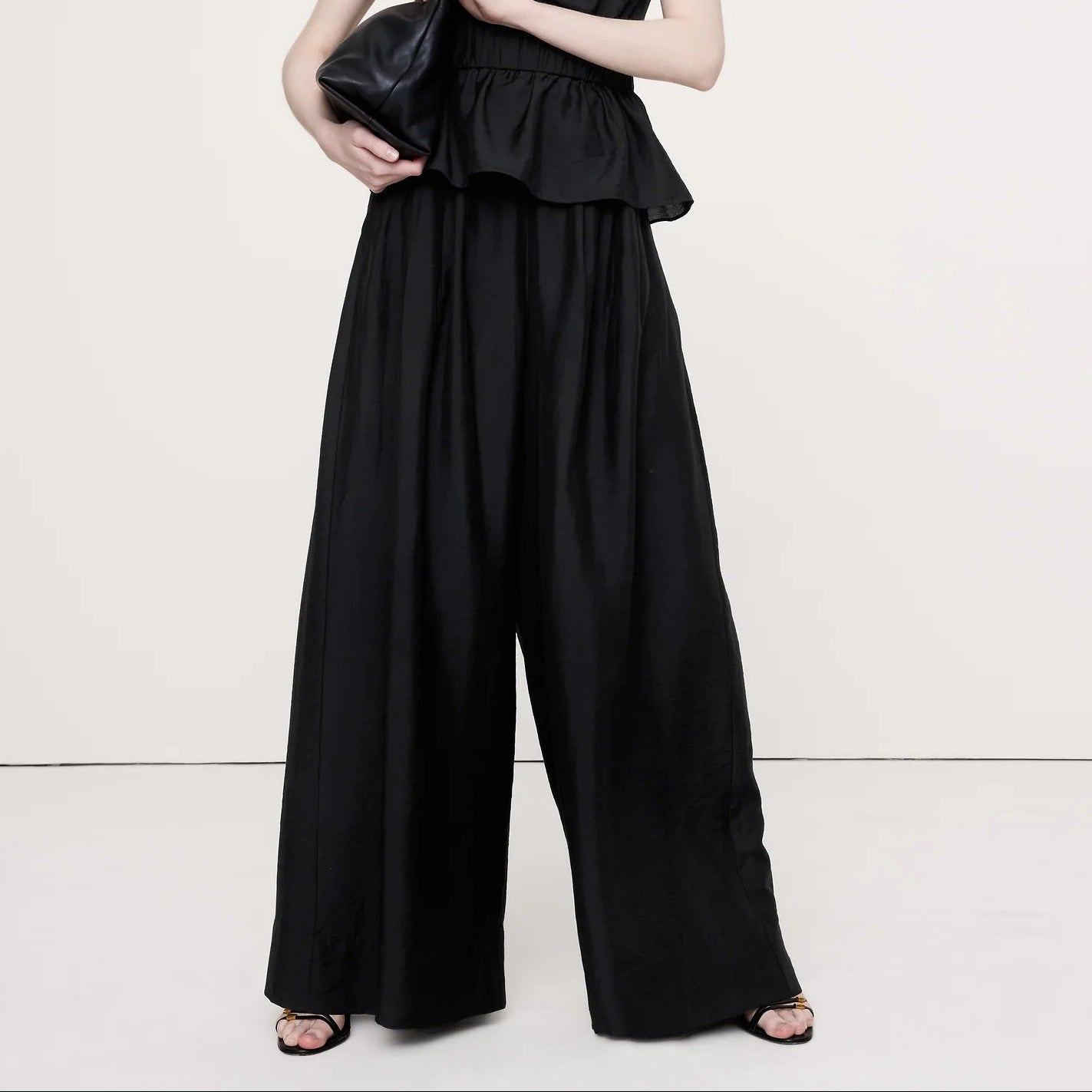 Woman wearing a black strapless jumpsuit holding a clutch on a white background