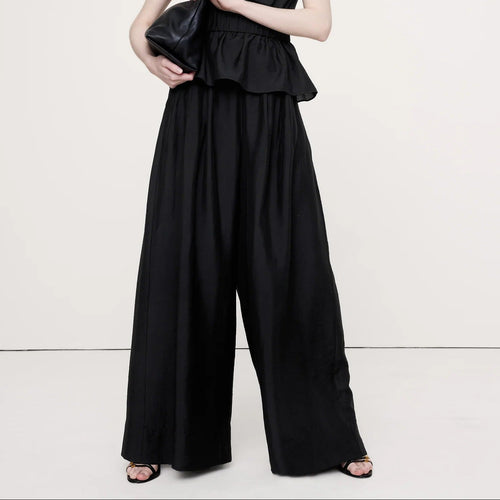 Woman wearing a black strapless jumpsuit holding a clutch on a white background