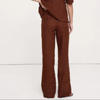 A model from behind wearing a matching brown linen-blend two-piece set consisting of a cropped long-sleeve top and wide-leg trousers, set against a plain white studio background.