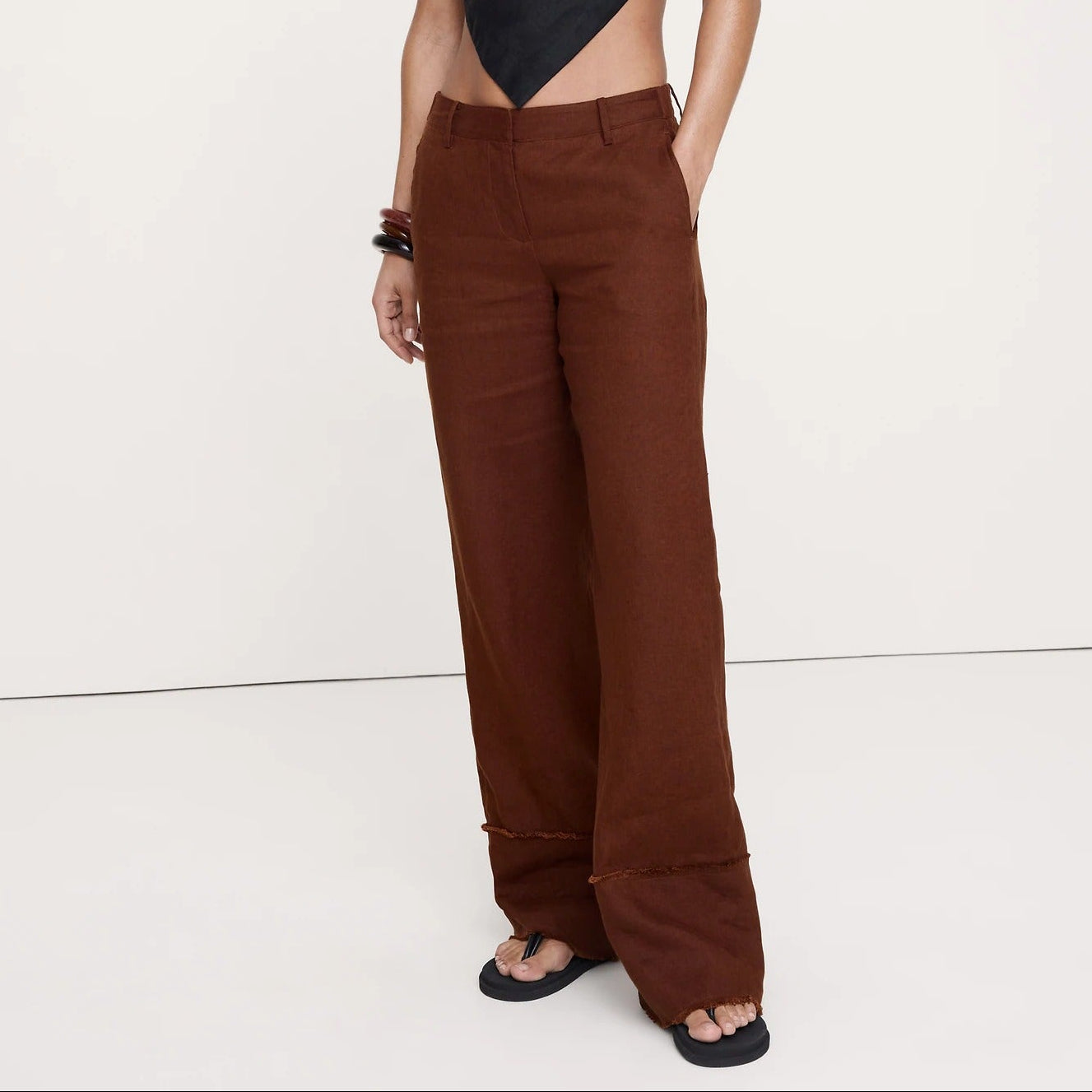 A model wearing a black halter-neck cutout top and brown wide-leg trousers, standing against a plain white studio background.