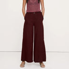 A woman modeling a sleeveless maroon knit top with a tie neckline and dark burgundy wide-leg trousers, standing against a plain white studio background.