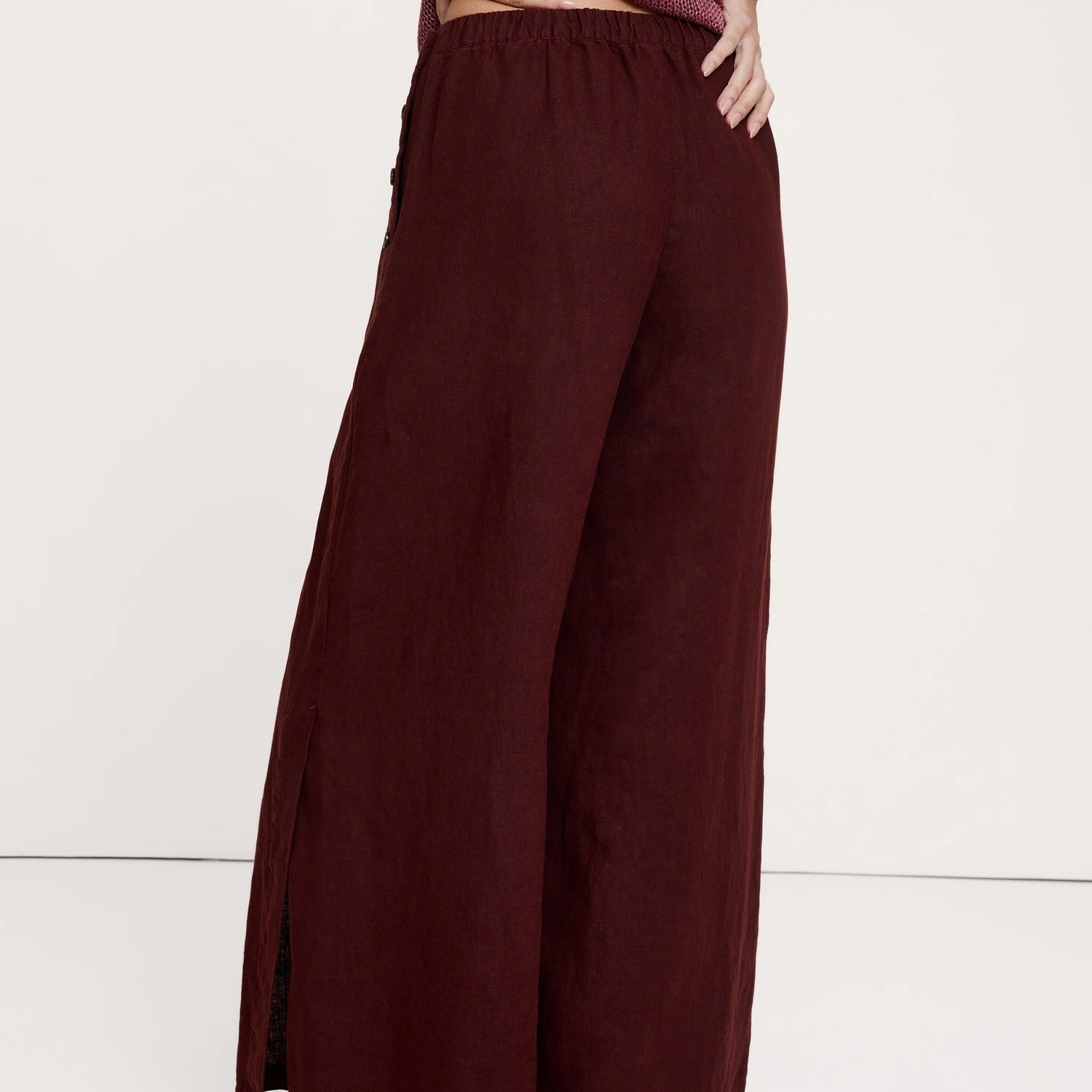 A person wearing wide-leg burgundy pants with side slits, paired with a textured mauve top and flat sandals, shown from the waist down against a plain light background.