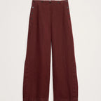 A pair of wide-leg trousers in a deep burgundy red, featuring decorative dark buttons along the outer seams of the legs, displayed flat against a light off-white background.