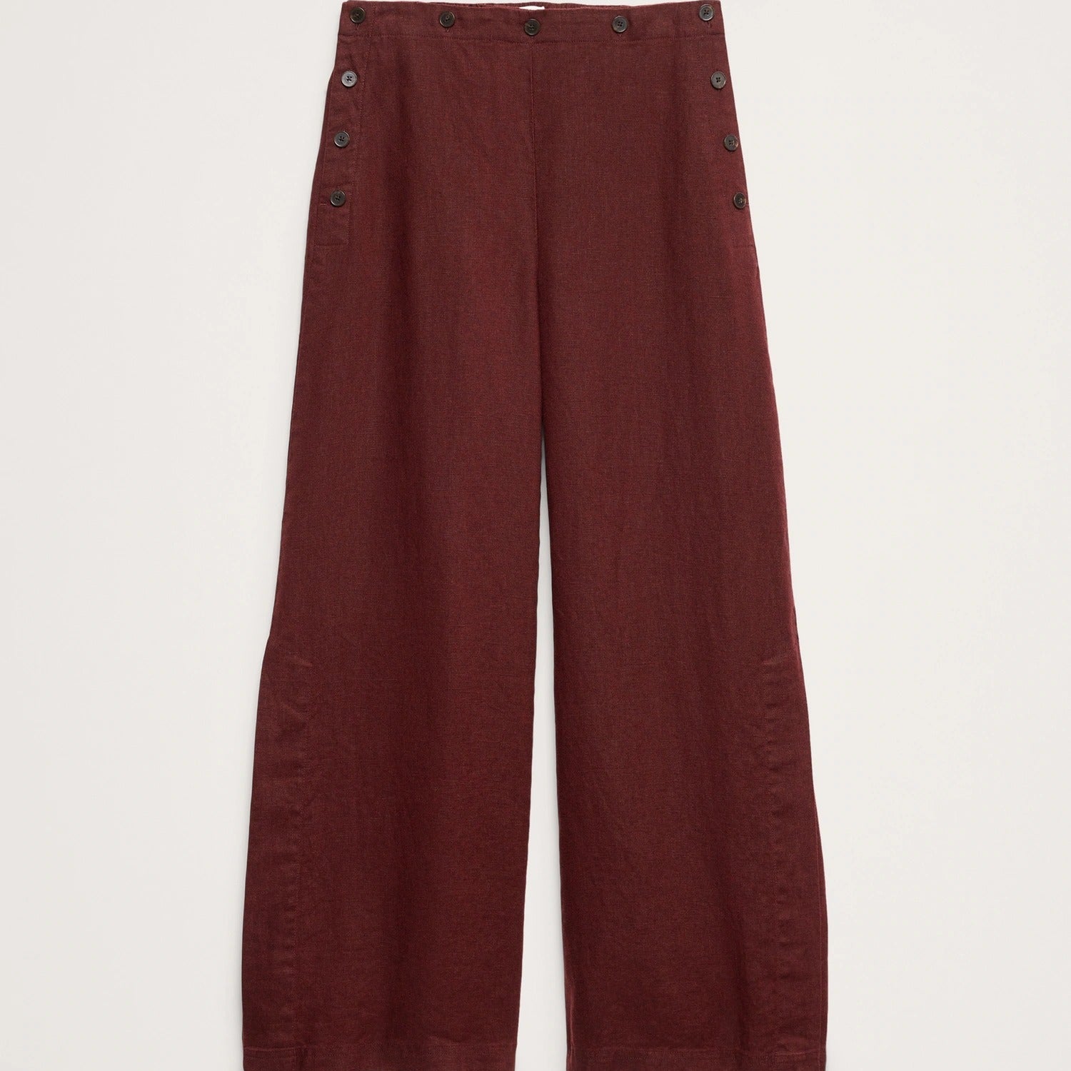 A pair of wide-leg trousers in a deep burgundy red, featuring decorative dark buttons along the outer seams of the legs, displayed flat against a light off-white background.