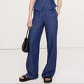 Woman wearing a blue jumpsuit holding a black handbag on a white background