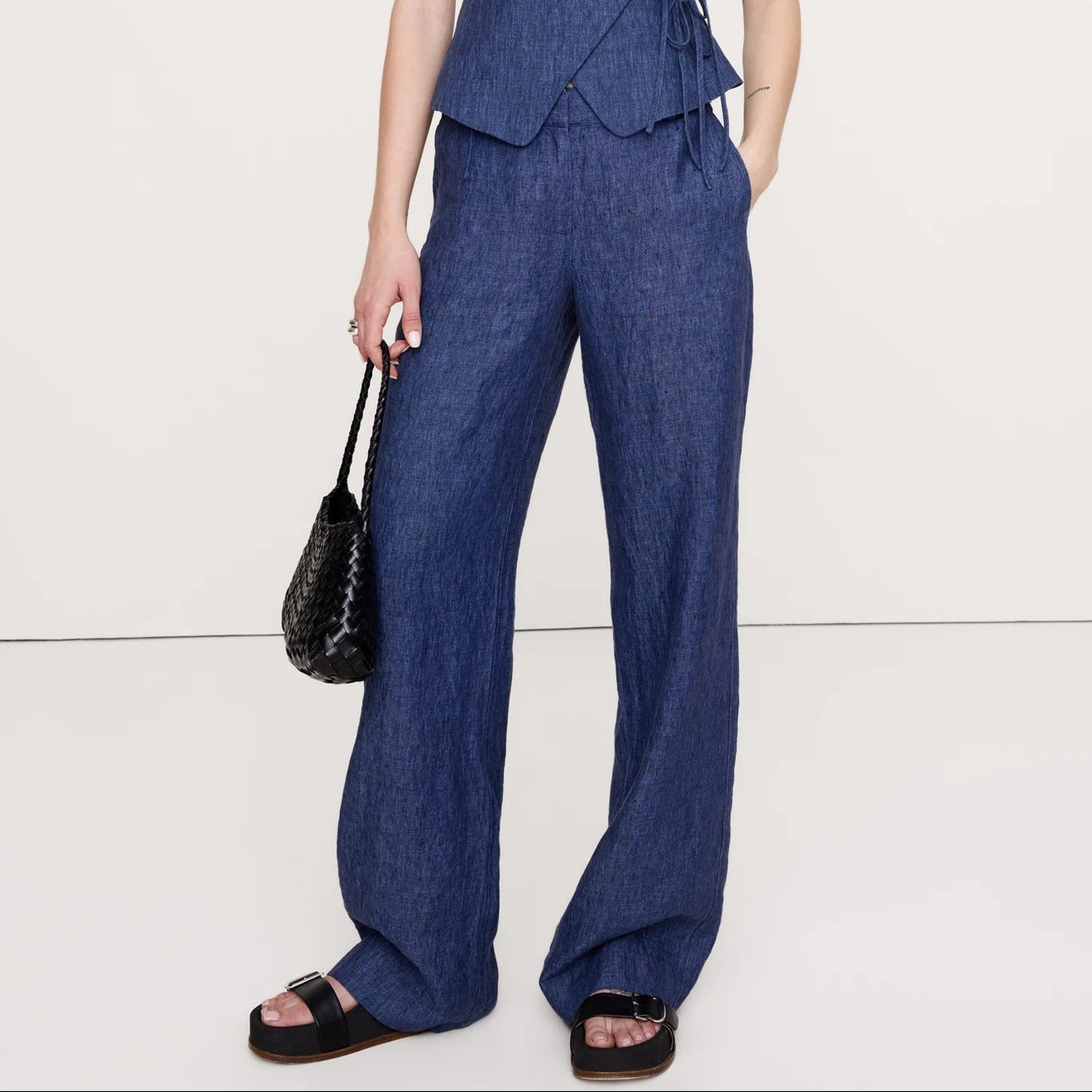 Woman wearing a blue jumpsuit holding a black handbag on a white background