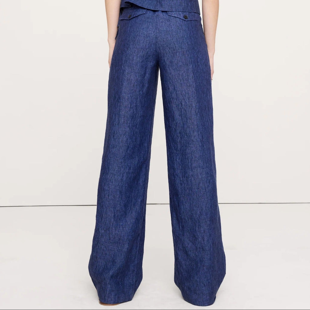 A woman viewed from the back wearing a sleeveless blue wide-leg jumpsuit against a plain white studio background.
