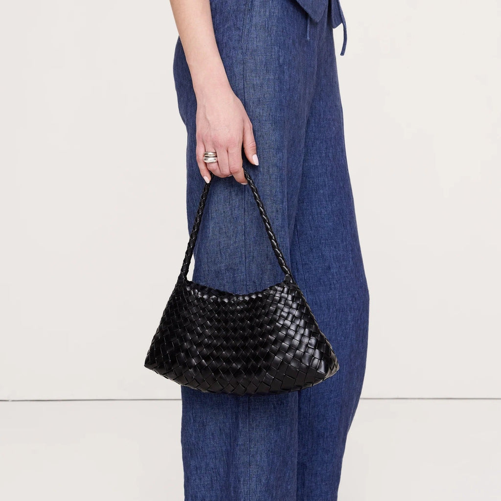 A person wearing blue wide-leg pants and black sandals holds a black woven leather shoulder bag with a braided strap against a plain light background.