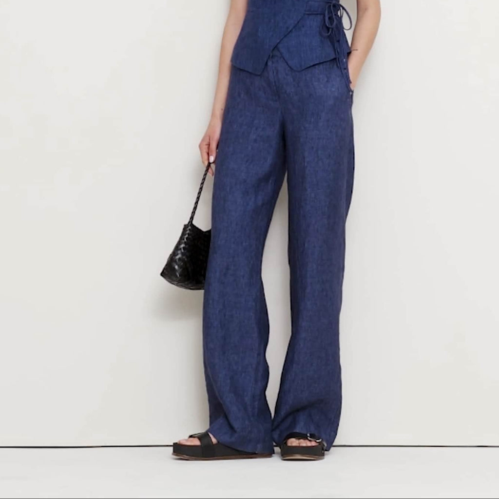 Woman wearing a blue jumpsuit holding a black handbag on a white background