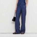 Woman wearing a blue jumpsuit holding a black handbag on a white background