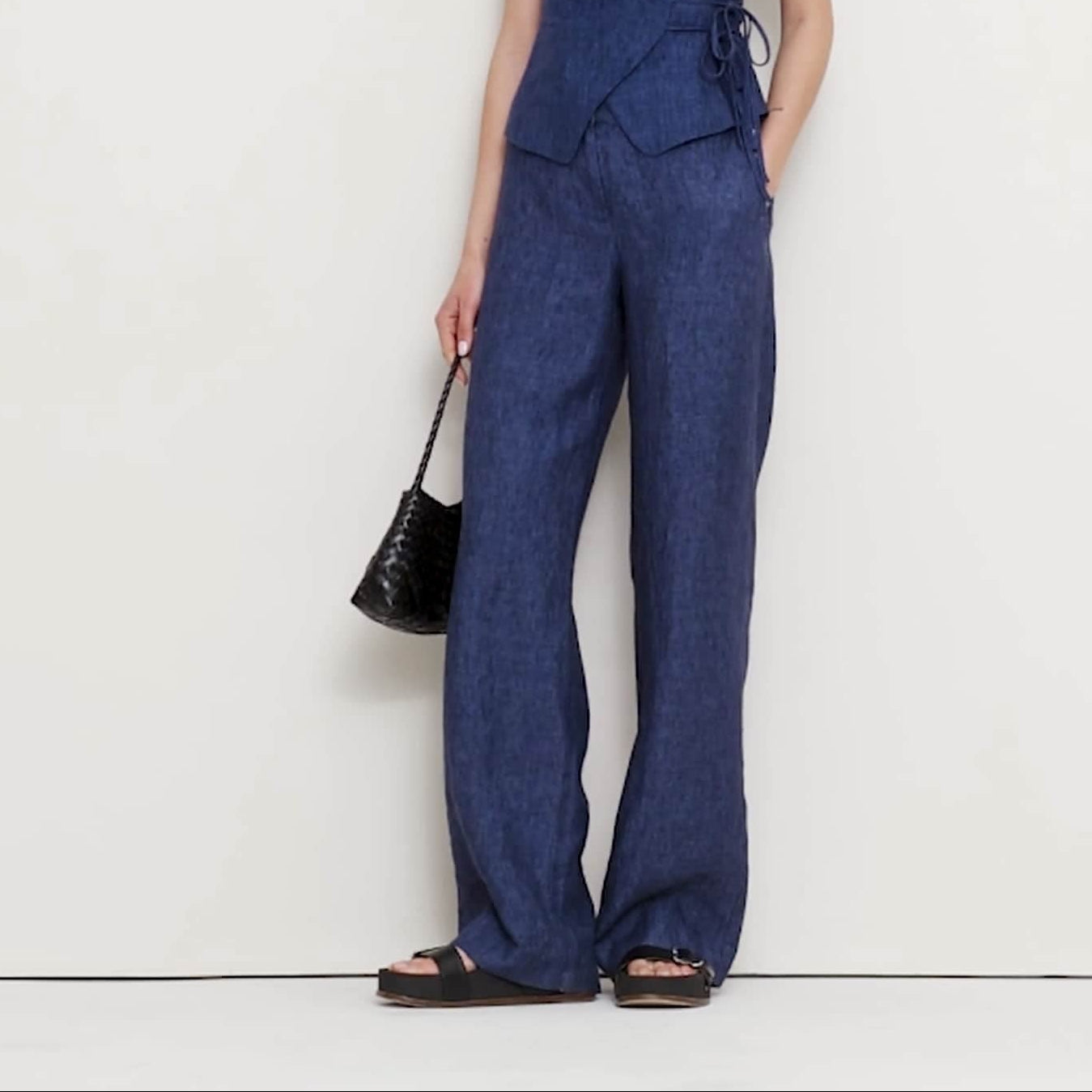 Woman wearing a blue jumpsuit holding a black handbag on a white background