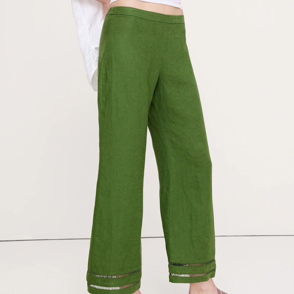 A person wearing olive green wide-leg linen pants with a white top and black flip-flop sandals, shown from the waist down against a plain off-white studio background.