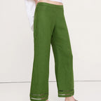 A person wearing olive green wide-leg linen pants with a white top and black flip-flop sandals, shown from the waist down against a plain off-white studio background.