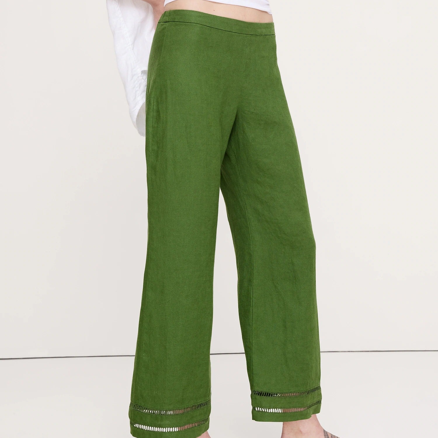 A person wearing olive green wide-leg linen pants with a white top and black flip-flop sandals, shown from the waist down against a plain off-white studio background.