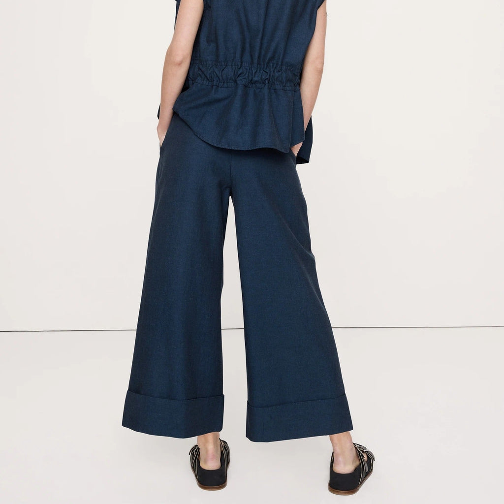 A woman shown from the back wearing a navy blue sleeveless top and matching wide-leg trousers, photographed against a plain light studio background.