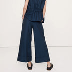 A woman shown from the back wearing a navy blue sleeveless top and matching wide-leg trousers, photographed against a plain light studio background.