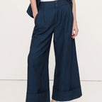 A person wearing dark navy wide-leg cropped pants with rolled cuffs, paired with a white top and black sandals, shown from the waist down against a plain light background.