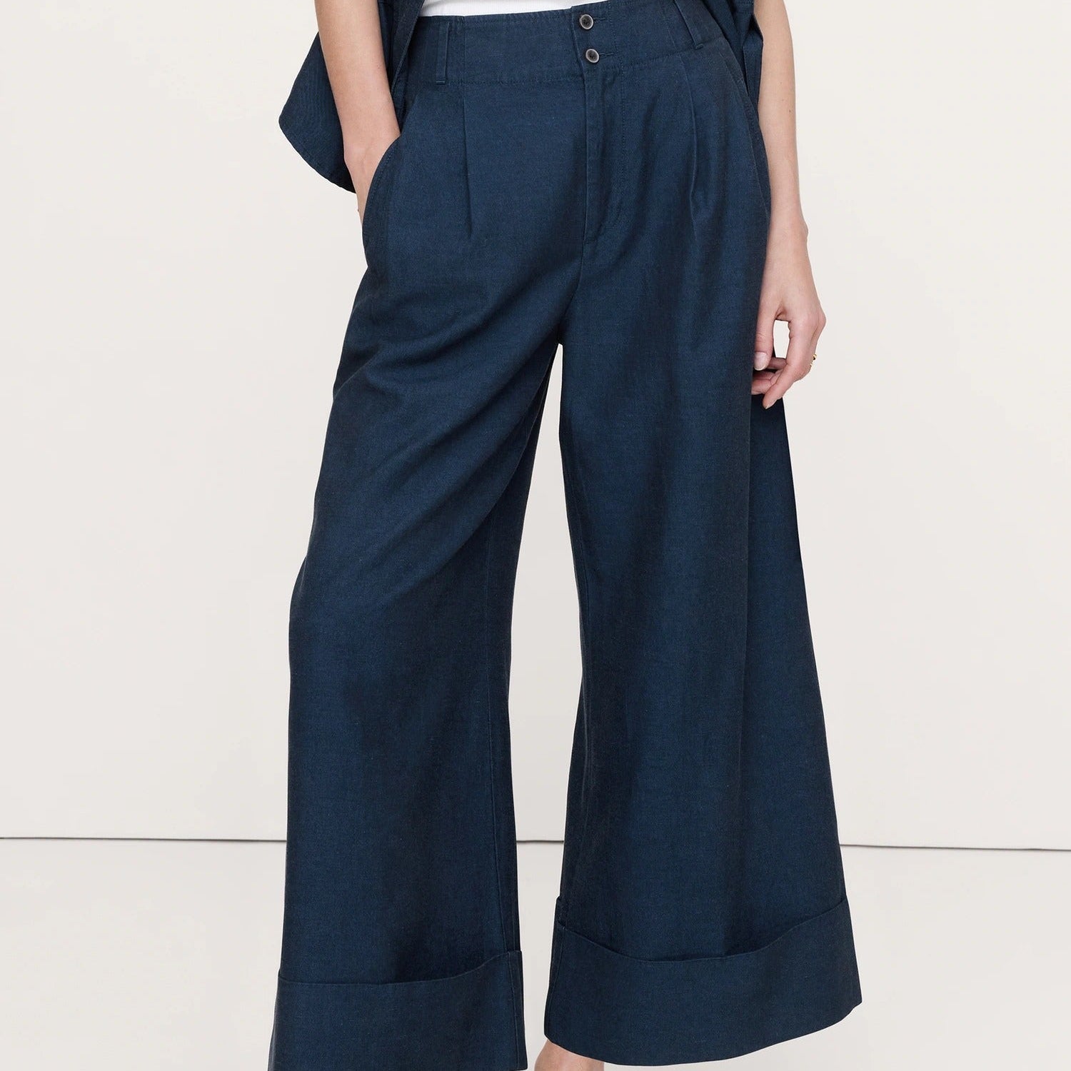 A person wearing dark navy wide-leg cropped pants with rolled cuffs, paired with a white top and black sandals, shown from the waist down against a plain light background.