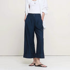 A woman modeling a pair of dark navy wide-leg cropped pants with a white tank top, white button-up shirt, and black flip-flops against a plain cream studio background.