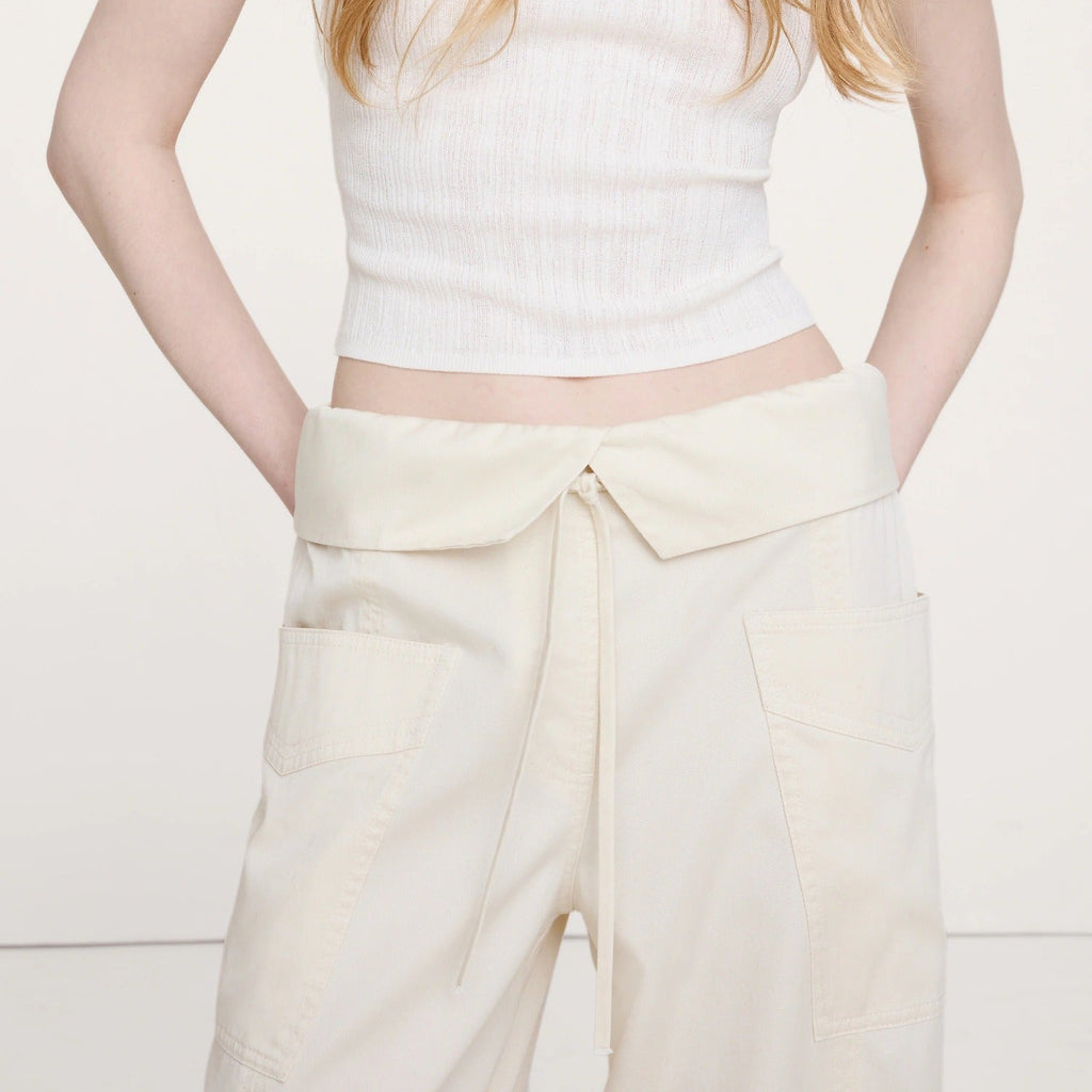 Person wearing a white sleeveless top and cream-colored pants on a light background