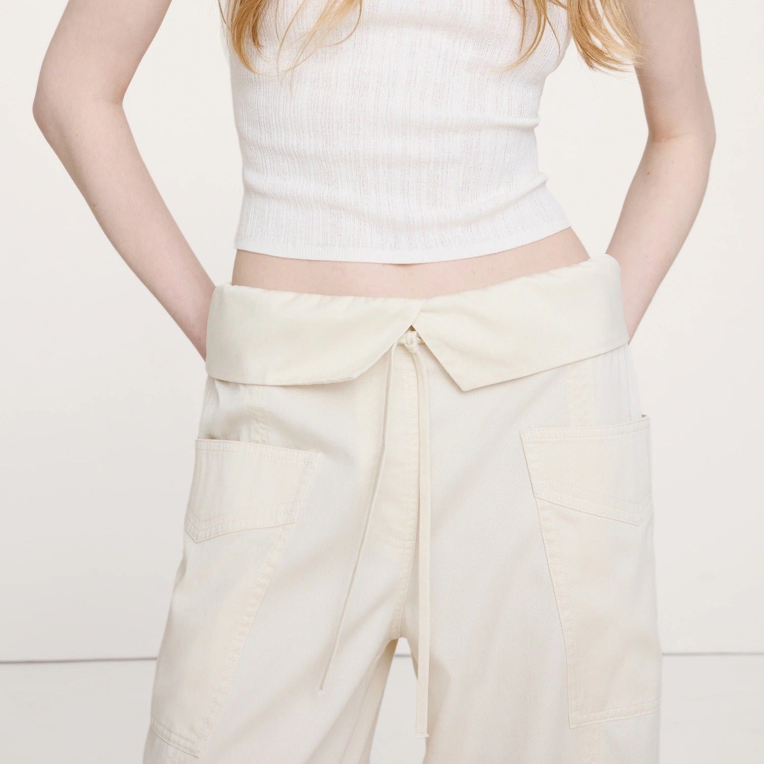 Person wearing a white sleeveless top and cream-colored pants on a light background