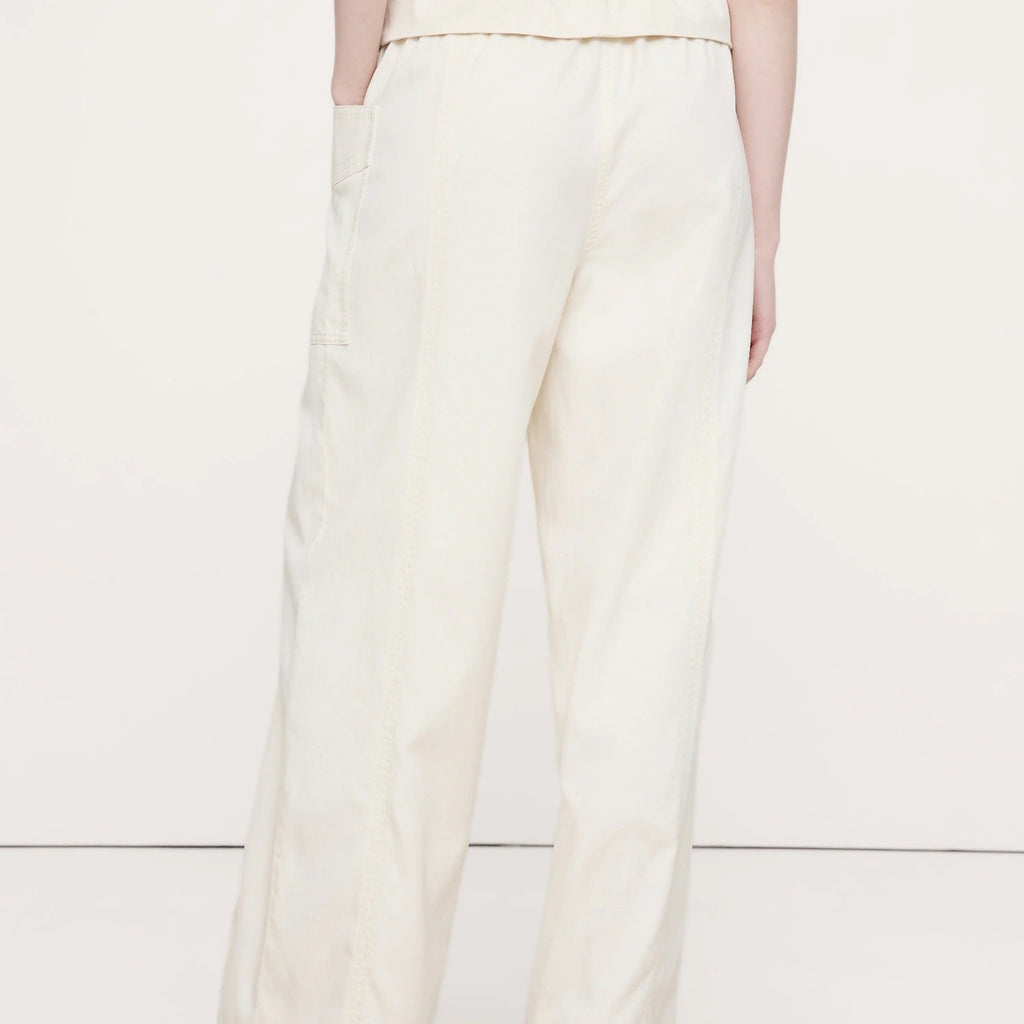 A person shown from the back wearing off-white wide-leg trousers with a gathered elastic waistband and side pockets, paired with a white ribbed top and black sandals, against a plain light background.