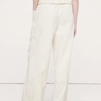 A person shown from the back wearing off-white wide-leg trousers with a gathered elastic waistband and side pockets, paired with a white ribbed top and black sandals, against a plain light background.