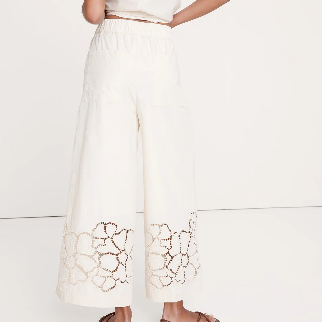 Person wearing a white outfit with intricate cut-out design on a plain background