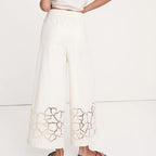 Person wearing a white outfit with intricate cut-out design on a plain background