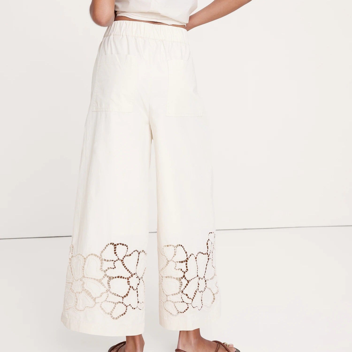 Person wearing a white outfit with intricate cut-out design on a plain background